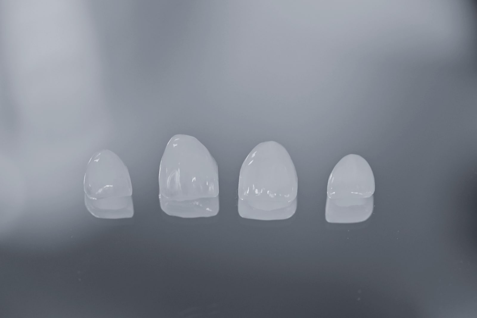 Four finished porcelain veneers photographed before placement, showing the translucency at the biting edge